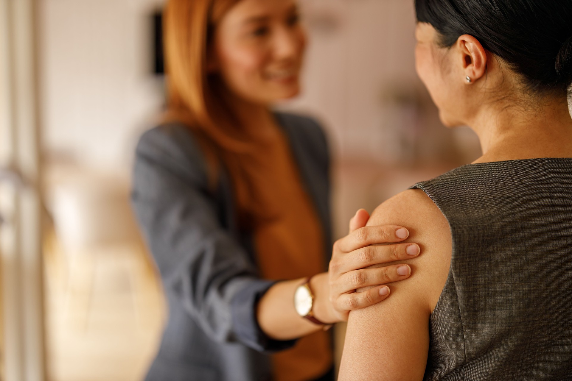 Businesswoman talking to colleague with hand on shoulder in supportive gesture at corporate workspace